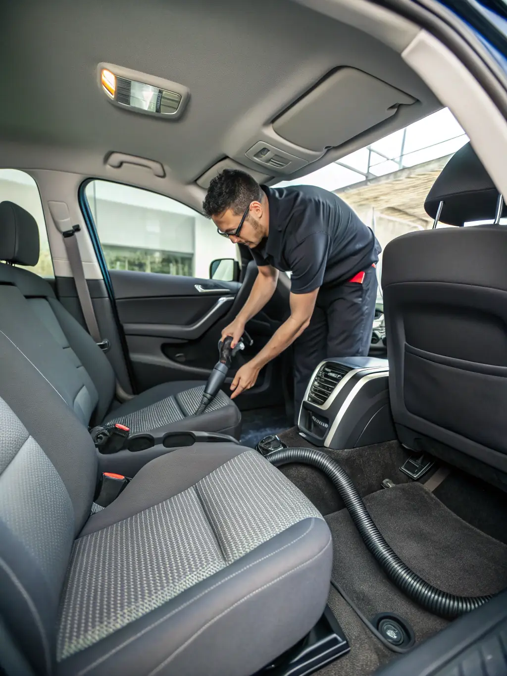 An image of a car interior being thoroughly vacuumed, with attention to detail on the carpets and upholstery. The lighting highlights the cleanliness and freshness of the interior.